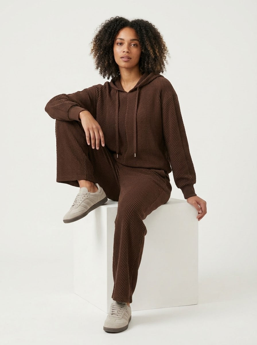 Model wearing chocolate Sunday pleated trousers, seated view