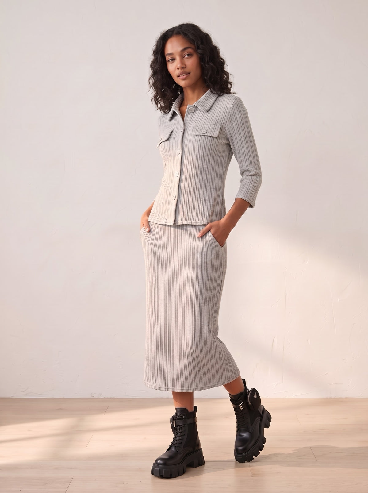 Model wearing Raya grey button-front pleated shirt and matching tube skirt, with sleeves pushed up and hands at the hips.