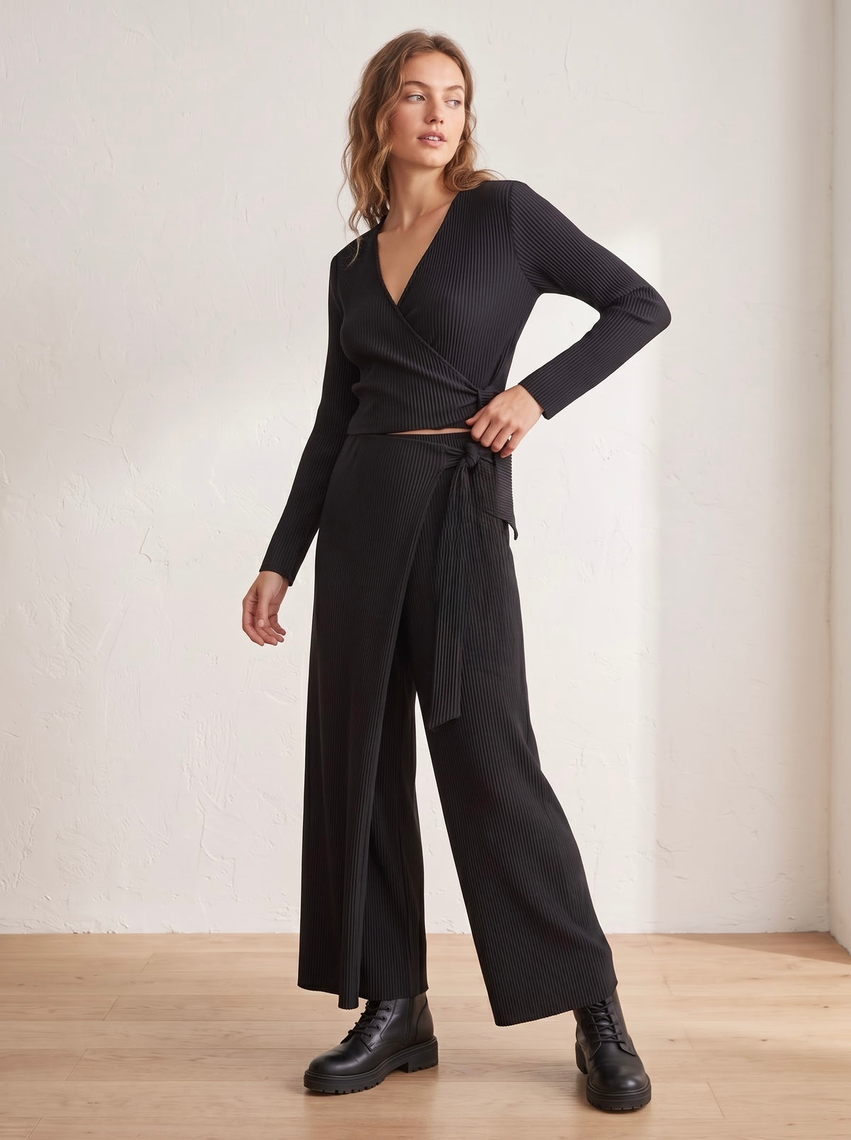 Model wearing Mina black pleated ballet wrap top and matching wide-leg trousers, showing the wrap-front panel and side tie.