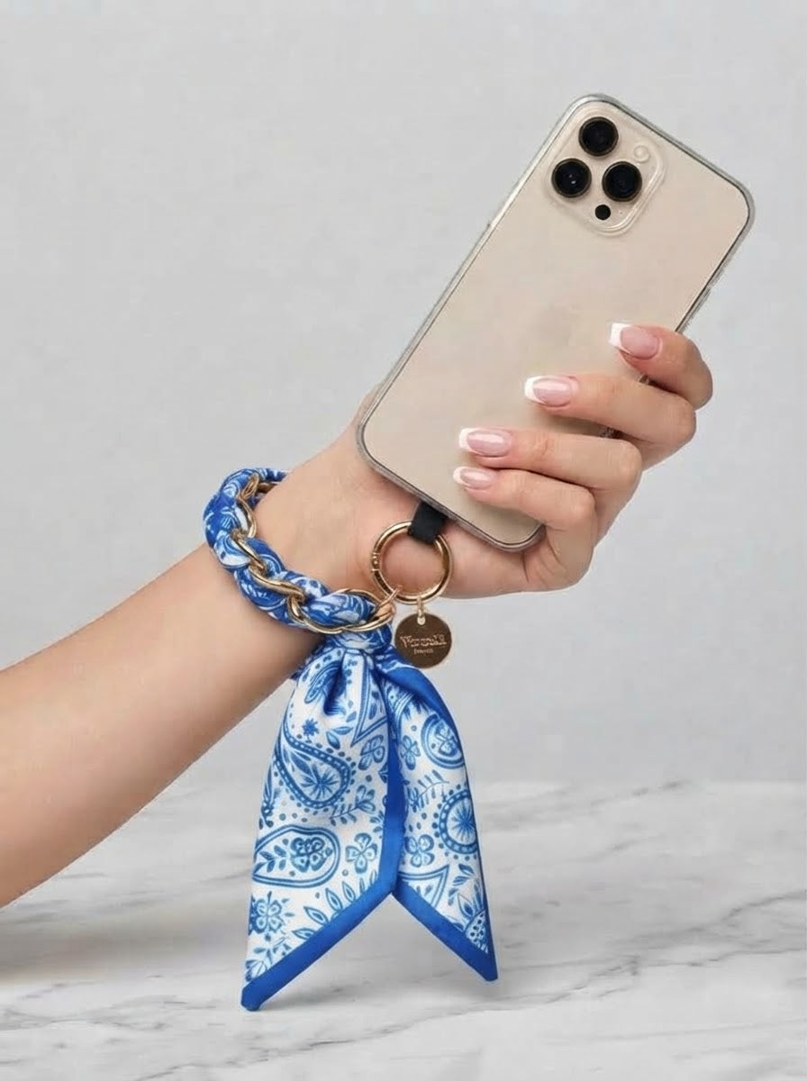 Blue Sandi paisley scarf print phone wrist strap worn around the wrist and attached to a phone case