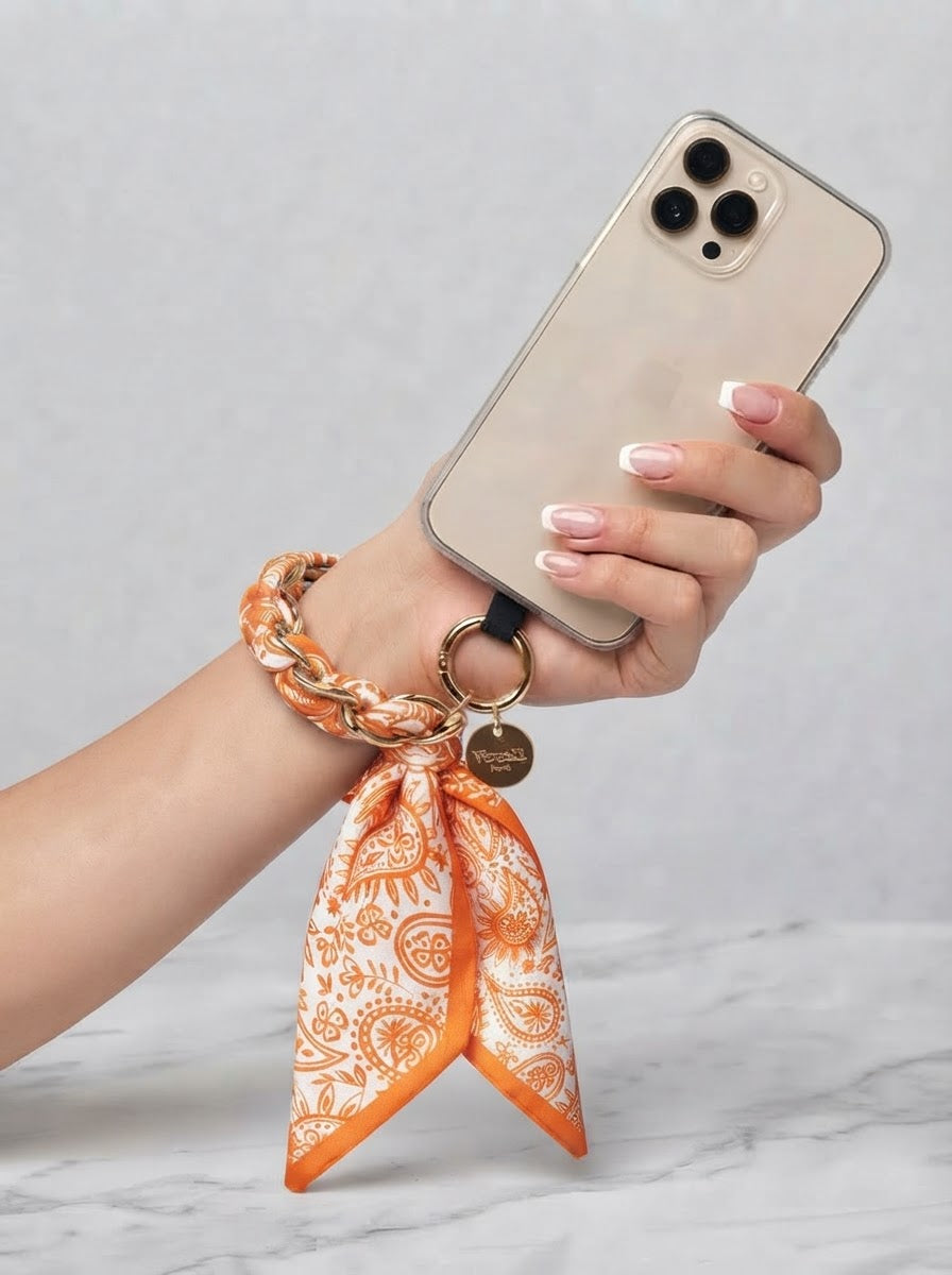 Orange Sandi paisley scarf print phone wrist strap worn around the wrist and attached to a phone case