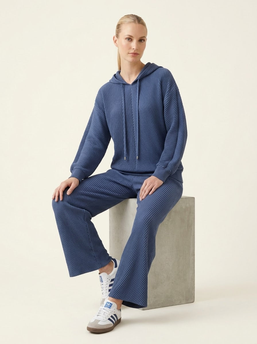 Model wearing Sunday pleated hooded top in navy, seated view