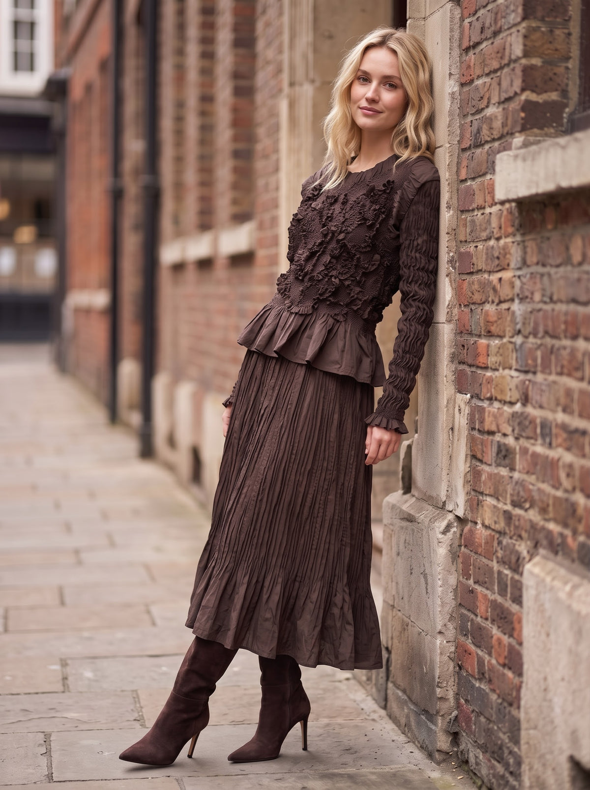 Model leaning against a brick wall in Emma chocolate Confetti Top and matching flared crinkle skirt with brown heeled boots.