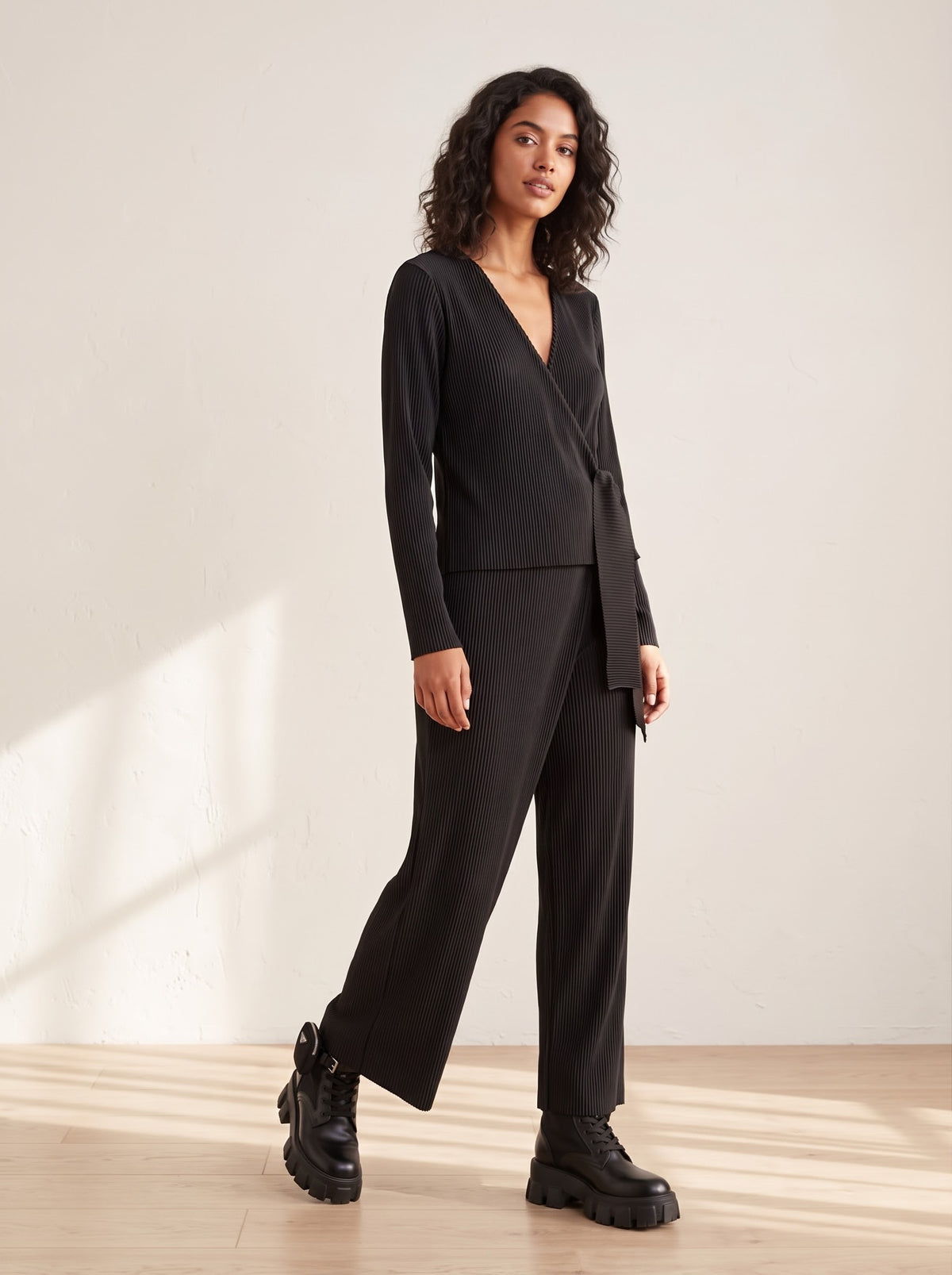 Model wearing Mina black ballet wrap top and matching pleated wrap-front trousers with wide side tie details and chunky boots.